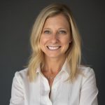 Ellen Rudofsky, PCC, CPCC smiling in a professional headshot, wearing a white button-up shirt against a dark gray background. She has shoulder-length blonde hair and a warm, approachable expression while facing the camera.